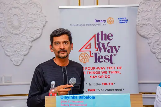 A speaker addressing the fellowship from the lectern beside the Four-Way Test banner.