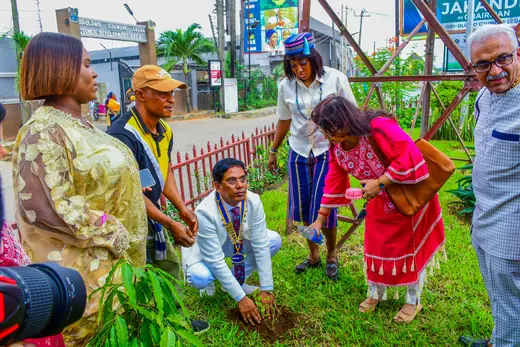 Members gathered around a sapling being planted on the grass, several helping at once.