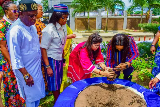 Two members lowering a sapling into the soil together while others watch.